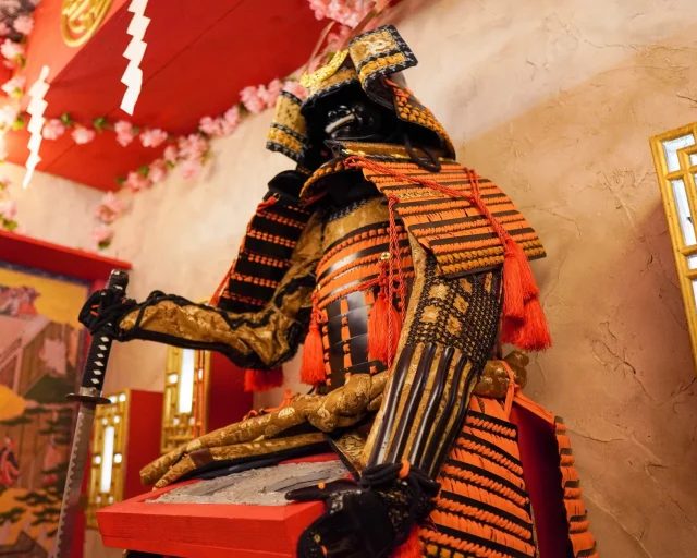 Samouraï en armure orange et noire près d'un paravent japonais rouge, salle Le masque du samouraï à Saint-Marcel