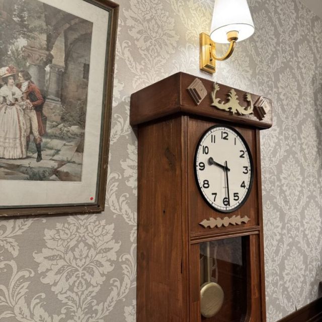 Horloge de parquet en bois sous une applique et un tableau ancien, décor des salles d'Escape Factory à Guérande