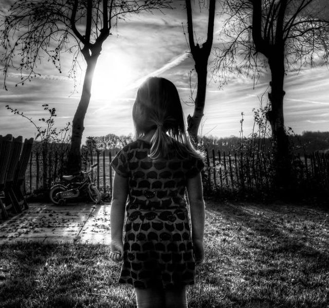 Enfant de dos dans jardin hivernal désolé, arbres nus et ciel gris, chez L'énigme à Rodez