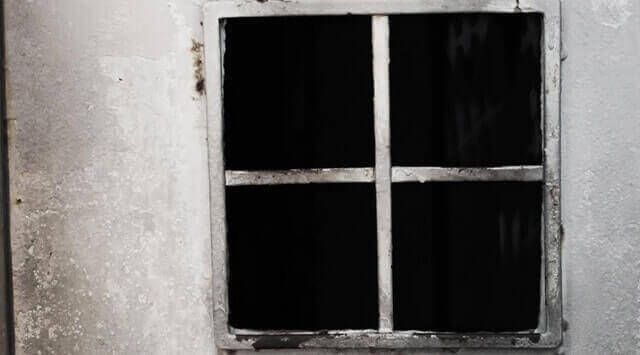Fenêtre grillagée à quatre carreaux dans décor urbain délabré, Prison Room chez Intrappola