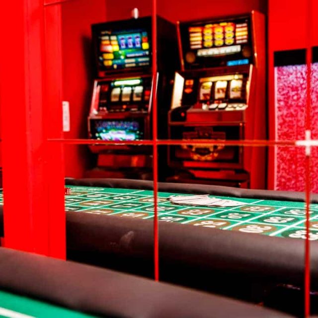 Décor de casino avec machines à sous illuminées, tapis de jeu vert et néon rouge chez Le Casino Magnifico