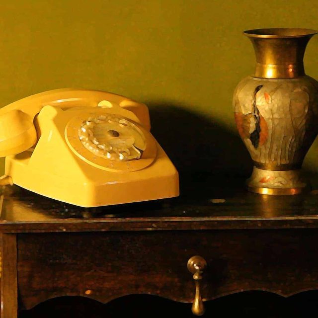 Téléphone jaune vintage et vase doré sur meuble ancien, décor de la salle Fouilles en cité Venete