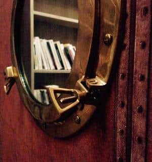 Hublot de navire en laiton ouvert sur des livres blancs, décor marin de Meurtre au Phare