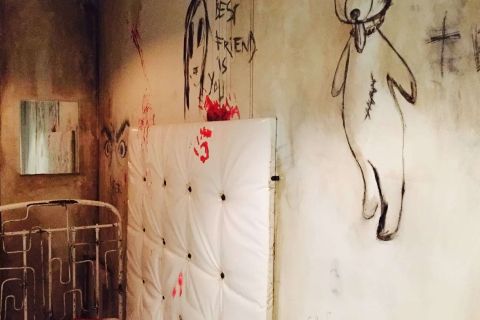 Chambre d'asile aux murs usés, dessins inquiétants et traces rouges, lit métallique rouillé