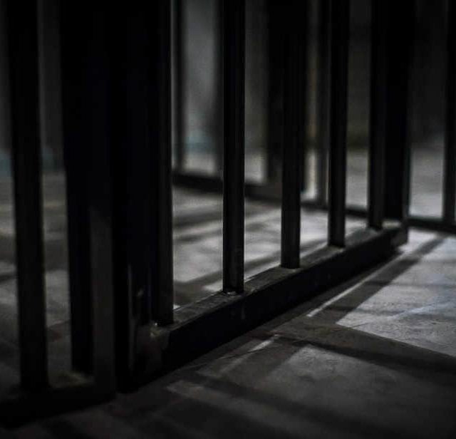 Couloir de prison souterrain avec barreaux métalliques et lumière zénithale, La Prison Bêta