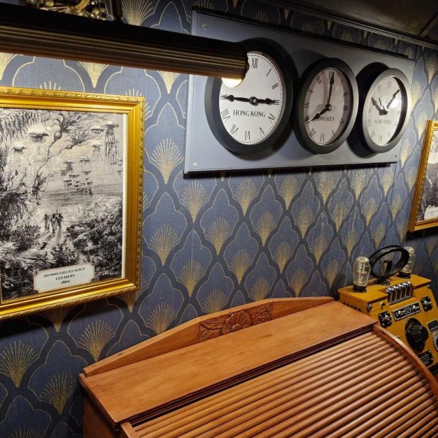 Murs bleu nuit à motif d'écailles, trois horloges, gravures encadrées et bureau à rideau, salle Sur les traces du magicien