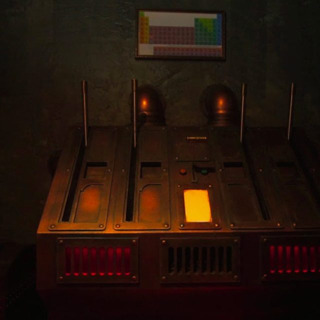 Machine à voyants rouges et orange sous un tableau périodique des éléments, salle Sherlock Holmes chez Freeing à Saint-Maximin