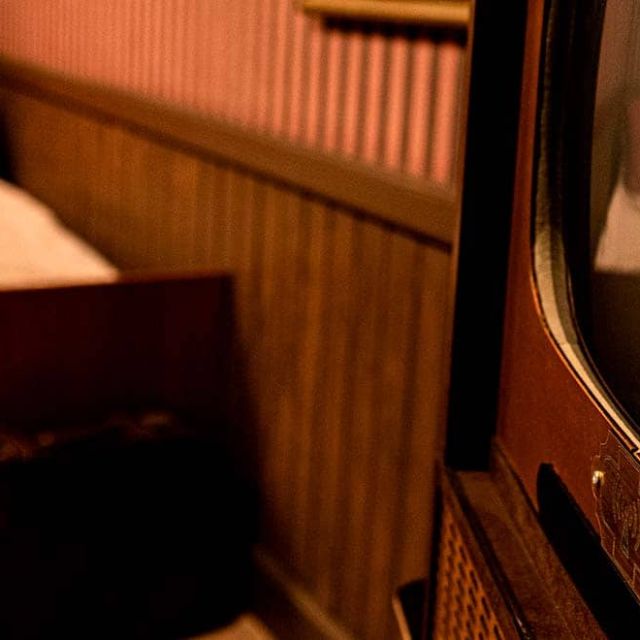 Chambre d'hôtel avec lit au coussin rouge et vieux téléviseur au premier plan, salle Sunhill Hotel chez Escape Time à Laval
