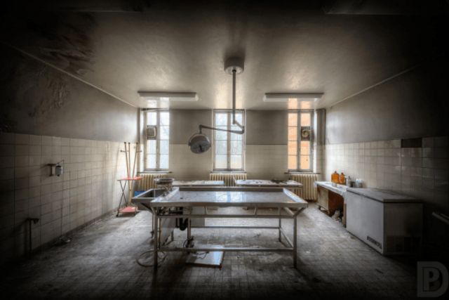 Salle d'opération délabrée avec table centrale et fenêtres, salle Le virus L.R chez Secret escape à Bourgoin-Jallieu