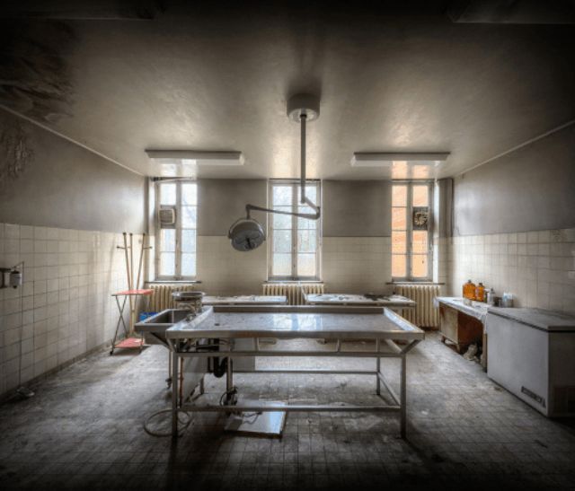 Salle d'opération délabrée avec table centrale et fenêtres, salle Le virus L.R chez Secret escape à Bourgoin-Jallieu