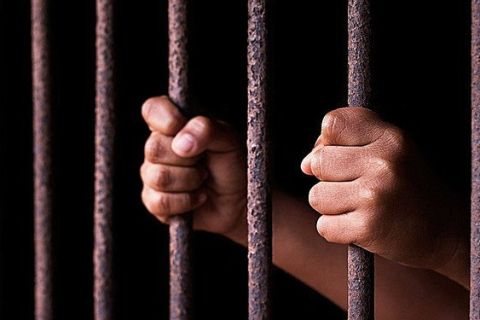 Mains agrippant des barreaux de prison rouillés dans l'obscurité