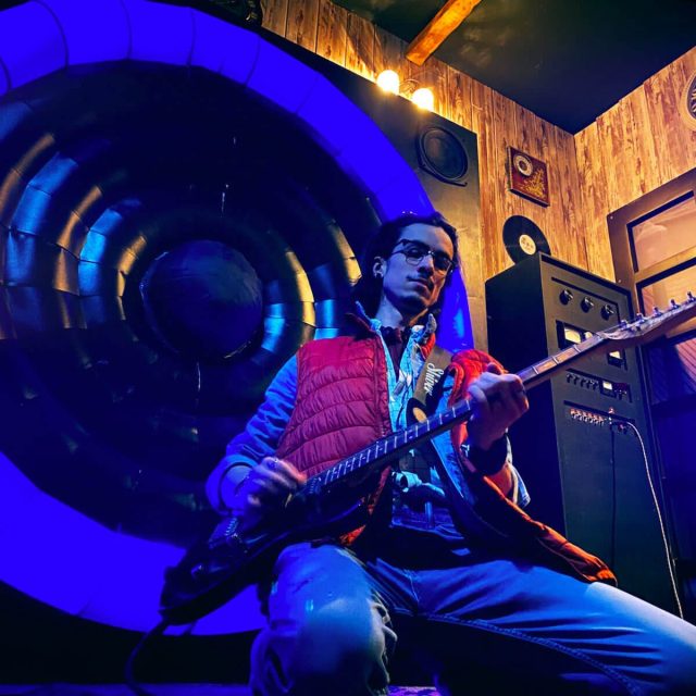 Joueur guitare à la main devant un grand tunnel lumineux bleu, salle Retour dans le temps chez Freeing à Saint-Maximin