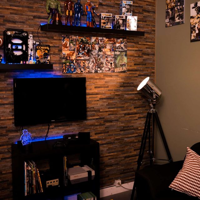 Salle thématisée avec panneaux pop culture, écran noir, figurines, affiche Star Wars encadrée d'une bande lumineuse bleue