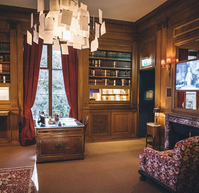Bureau de boiseries avec bibliothèque, cheminée, rideaux rouges et lustre de papier, enseigne Cantal'Enigme à Aurillac