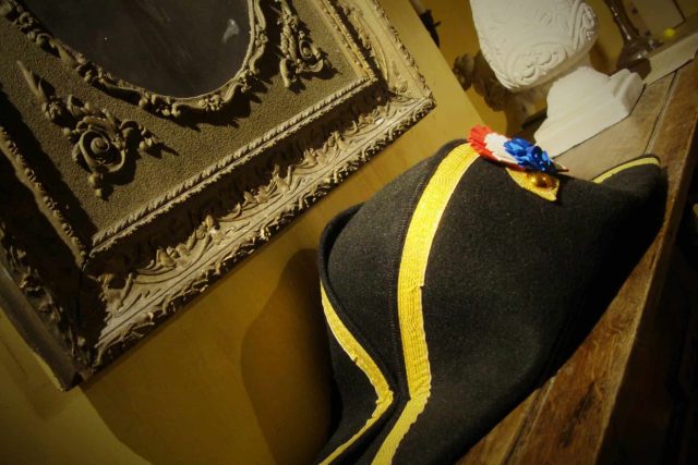 Bicorne noir avec ruban jaune et broche tricolore, plâtres ornementaux, décor époque Napoléon chez Prizoners Fréjus