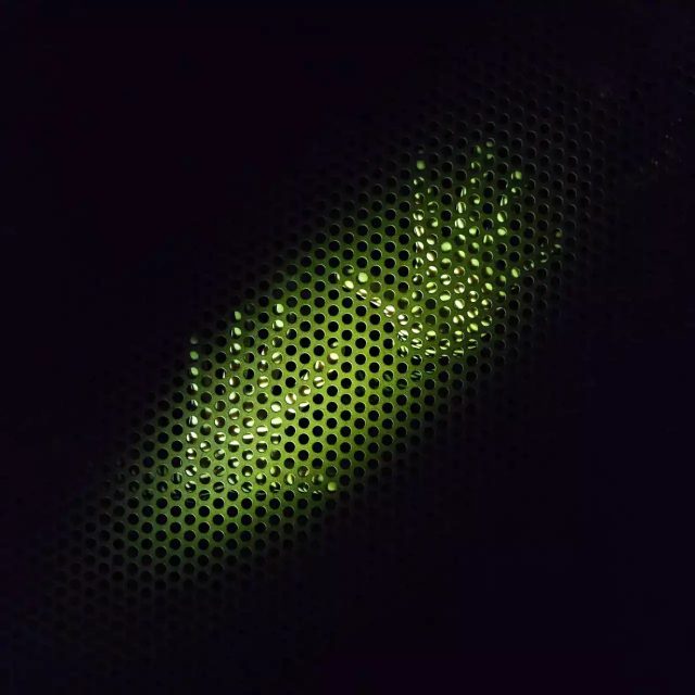 Grille métallique perforée illuminée en vert fluo sur fond noir, ambiance technologique de la salle L'inquiétant professeur Tychsen