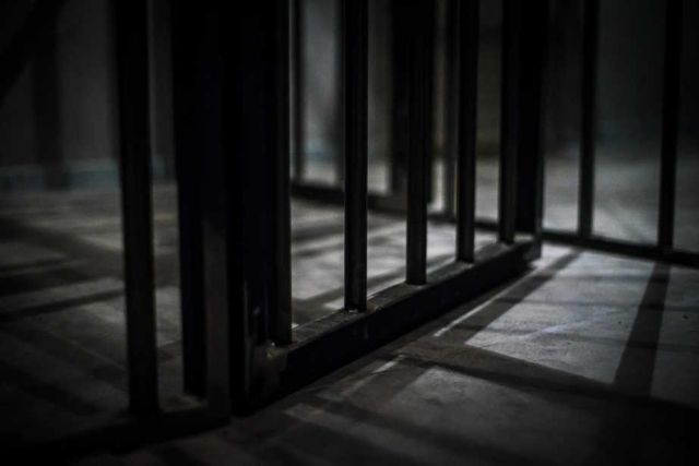 Couloir de prison austère aux barreaux métalliques et sol bétonné, éclairage cru dans La Prison Bêta