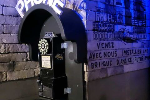 Cabine téléphonique avec enseigne Phone sur un mur de brique bleuté, salle Comics City chez Captive à Clichy