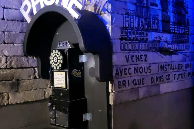 Cabine téléphonique avec enseigne Phone sur un mur de brique bleuté, salle Comics City chez Captive à Clichy