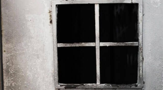 Fenêtre sombre à croisillons dans un mur blanc décrépi, visuel d'Intrappola