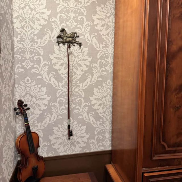 Violon posé dans un coin devant un papier peint à motifs gris, décor des salles d'Escape Factory à Guérande