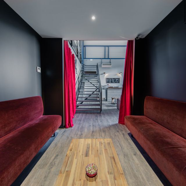 Banquettes rouges en vis-à-vis menant à un escalier métallique, espace d'accueil de Spirit Game à Douvaine