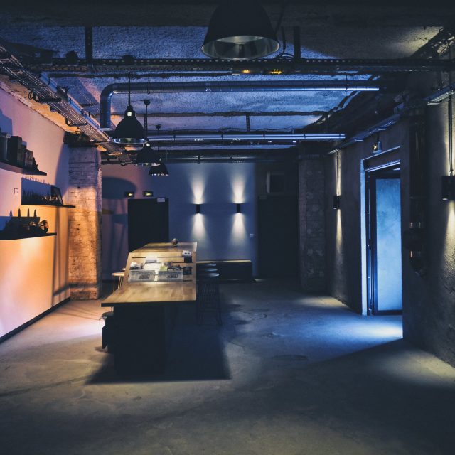 Espace industriel aux murs de pierre, éclairage bleu et orange, mobilier noir minimaliste chez Les Secrets du Sablier à Strasbourg
