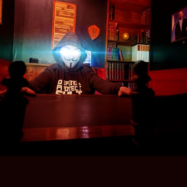 Personnage masqué luminescent face à deux joueurs dans un décor rouge et noir aux Arcanes du Pouvoir