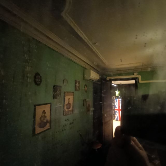 Couloir délabré aux murs verts écaillés, portraits anciens, lumière rougeâtre, chez Time Out Real Escape Game à Marseille