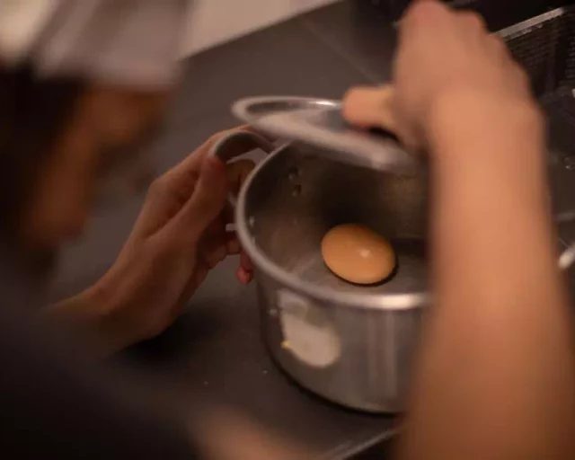 Mains soulevant le couvercle d'une casserole contenant un oeuf, salle Panique en cuisine chez Gaillard Académie à Brive