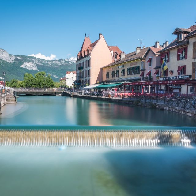 Rivière turquoise avec petit barrage et rangée de maisons colorées devant les montagnes, Hunting Town à Annecy