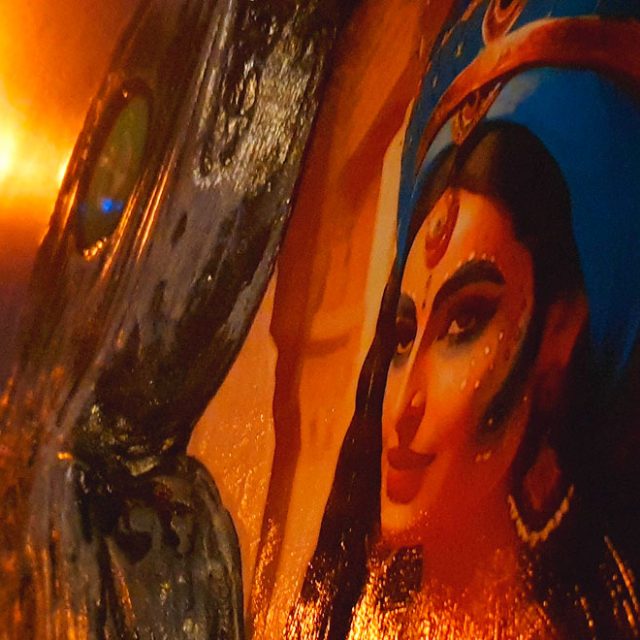 Fresque d'une femme au turban bleu sous une applique allumée, tons orangés, salle Mirage chez Escape Time à Barjouville