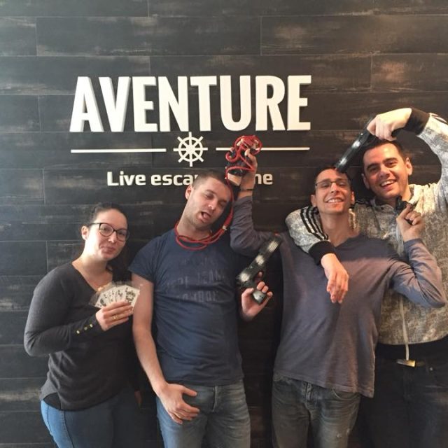 Cinq joueurs célèbrent leur évasion devant le logo d'Aventure Live Escape Game à Nice