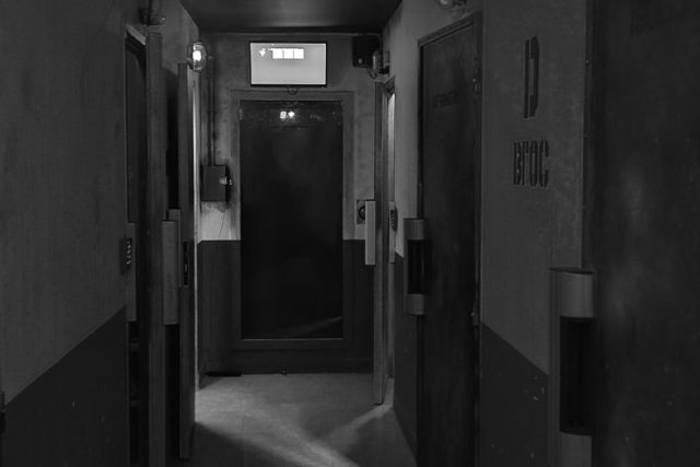 Couloir sombre d'une prison avec portes métalliques et affichage lumineux