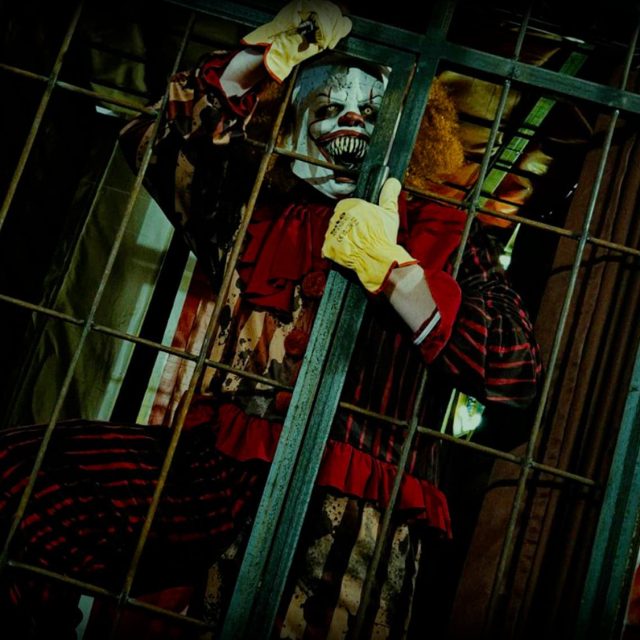 Clown maquillé derrière les barreaux d'une cage verte, salle Le cirque hanté chez Freeing à Saint-Maximin