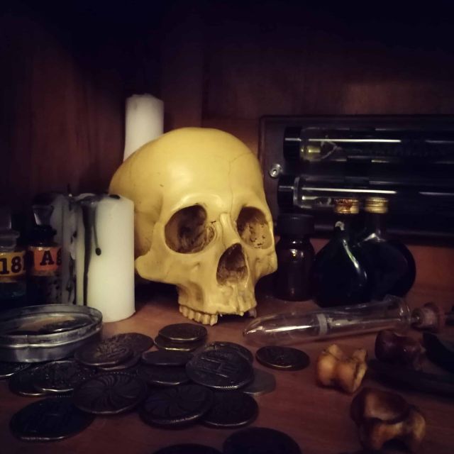 Crâne jauni, bougies et pièces anciennes sur une étagère de bois, salle Dracula chez Hint Hunt à Paris