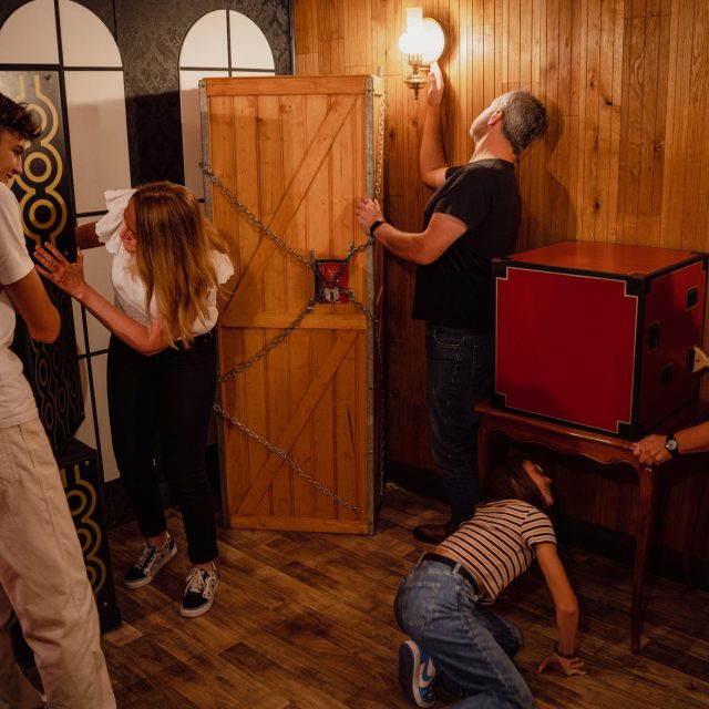 Quatre joueurs manipulent une porte chaînée et des objets dans un décor en bois chaleureux chez Steam Escape Limoges