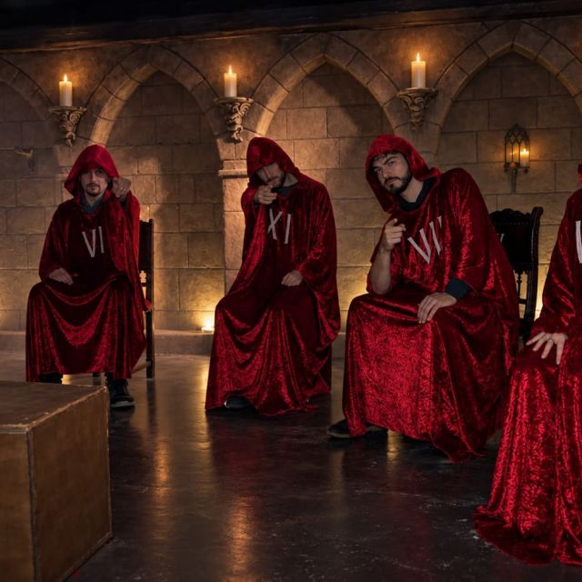 Cinq personnages en capes rouges numérotées assis dans une crypte à bougies, salle La Menace des Loups, Wolf Gang