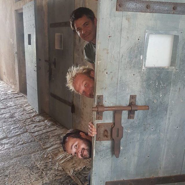 Visages qui dépassent d'une porte de cellule en fer entrouverte, salle La grande évasion au Fort Teremba à Moindou
