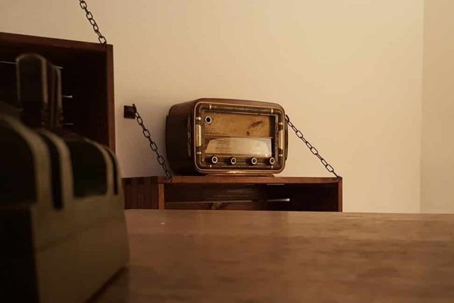 Vieille radio posée au bout d'un bureau en bois près d'un mur clair, salle Le bureau du général chez La Cellule