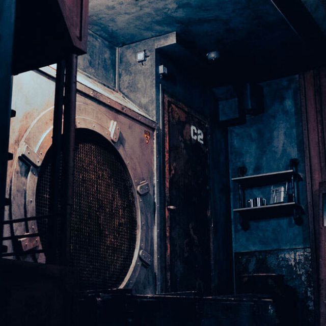 Pièce industrielle très sombre aux machines à peine visibles, salle Alpha District chez Escape Time à Mulsanne
