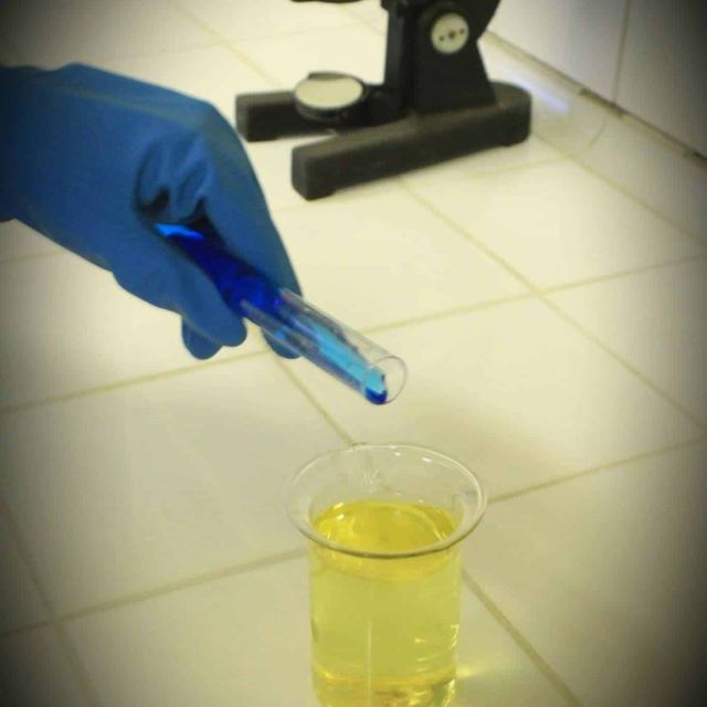 Main gantée versant un liquide bleu dans un tube à essai jaune au laboratoire