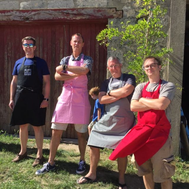 Quatre joueurs en tabliers colorés posent devant une porte rouge dans la cour de Escape Game Oeno-Logic Blaye