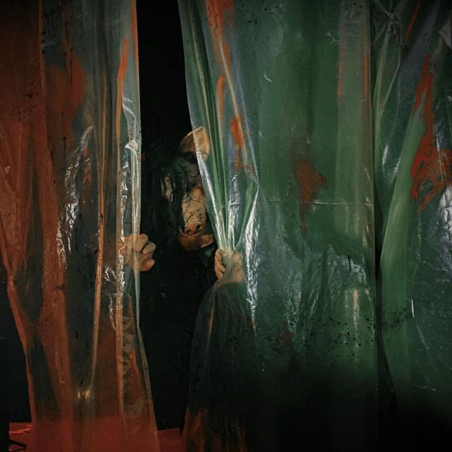 Joueurs face à des murs de tôle rouille et verte dans l'atmosphère d'horreur de The Saw Massacre