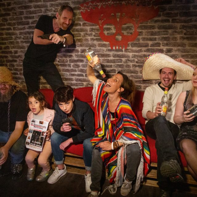 Groupe de joueurs célébrant dans un décor avec briques rouges, logo crâne rouge, accessoires festifs chez The Box Escape Games à Metz