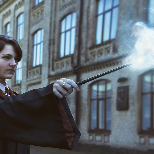 Jeune sorcier en uniforme brandissant une baguette magique devant un château
