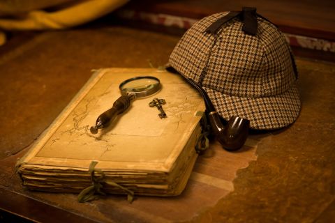 Loupe, clé, journal et casquette victorienne sur table en bois sombre, chez Mission Sherlock à Gentilly