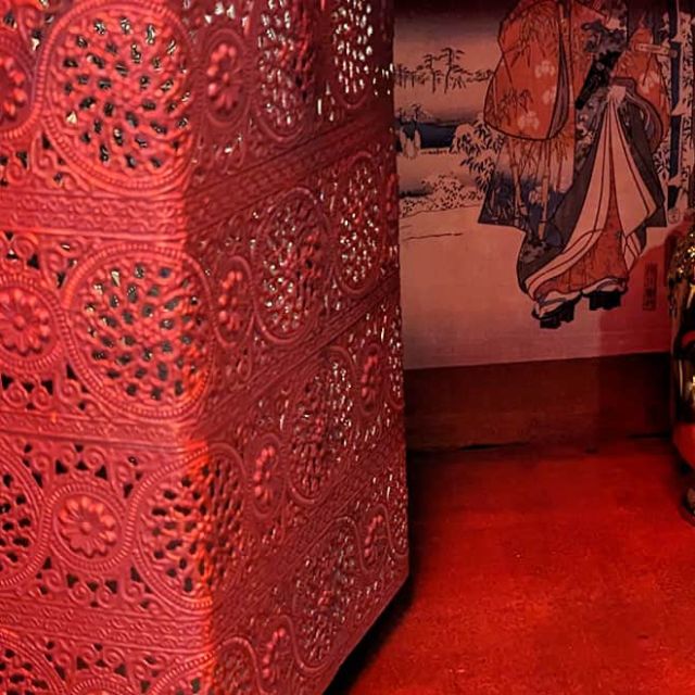 Tête de Bouddha rouge près d'une cloison ajourée et d'estampes, éclairage rouge, salle Mission Tokyo chez Escape Time