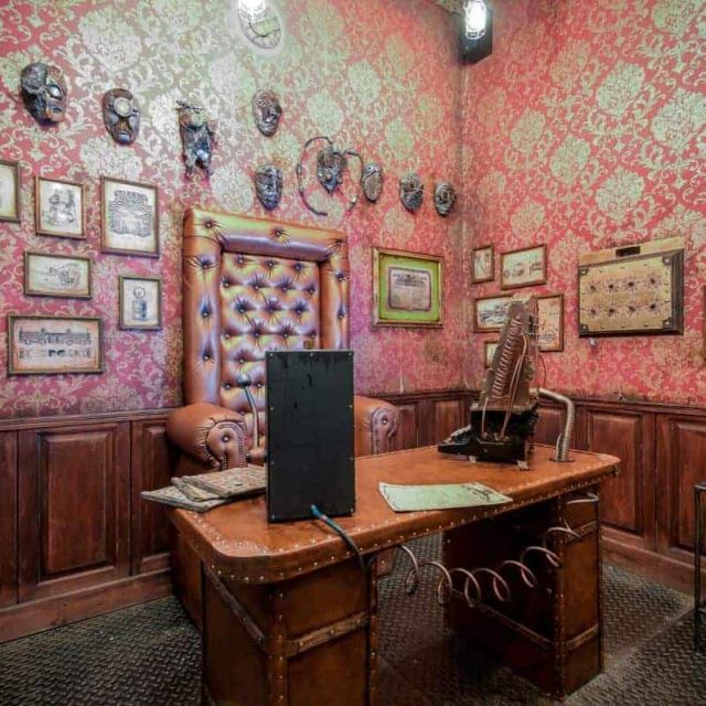 Bureau victorien aux murs rose fuchsia, masques tribaux et cadres anciens, bureau en cuir clouté chez Escape the Cage