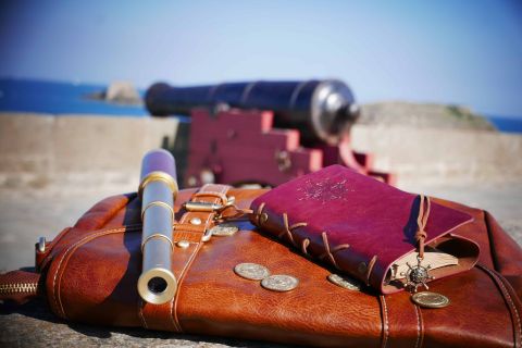 Accessoires de pirate : lunette, télescope, pièces d'or, journal, canon en arrière-plan, mer bleue